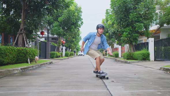 Asian active hipster athletic guy enjoy ride Surf Skate Board on street in front of his house.