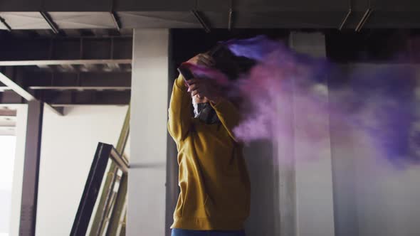 Mixed race woman holding blue and purple flares standing in an empty building