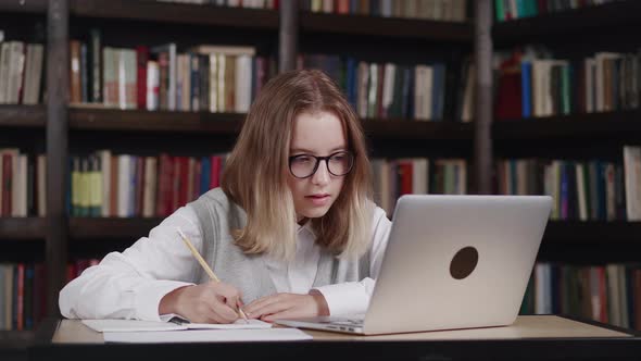 Girl Wearing Glasses Doing Homework Schoolgirl Studying Online Using Laptop Making Notes in Copybook