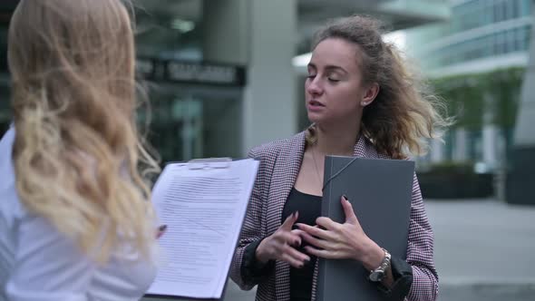 Young woman discussing plans and documents with colleague near office building