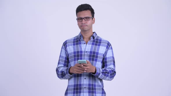 Happy Young Indian Hipster Man Thinking While Using Phone