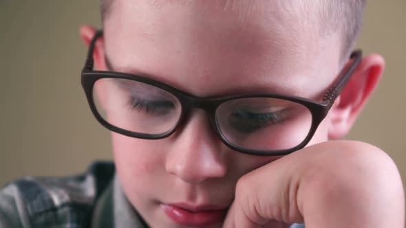 Close-up face of a caucasian boy wearing glasses 5-7 years old diligently doing homework, a child we