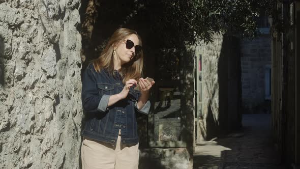 Smiling brunette woman  in sunglasses uses her phone in the city.