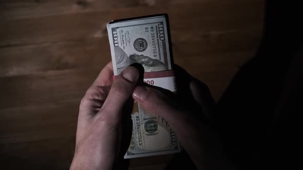 Male Hands Hold Three Stacks of 10000 US Dollar Bills on Wooden Background