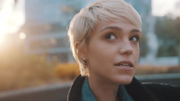 Portrait of Young Caucasian Woman with Short Blond Hair Winking in the City Park