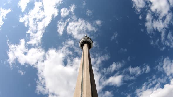 Upward view of CN tower against blue sky with clouds. Time lapse