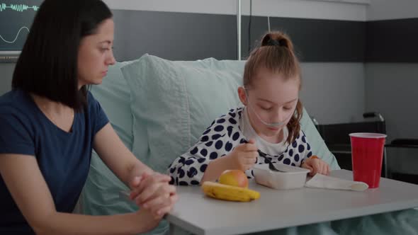 Mother Sitting with Sick Daughter While Eating Healthy Food Meal in Hospital Ward