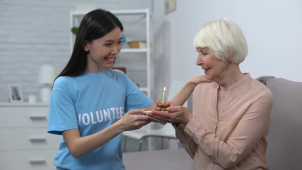 Smiling Volunteer Presenting Birthday Cake to Senior Pensioner in Nursing Home