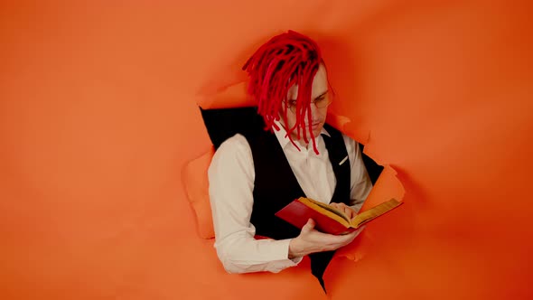 Well Dressed Man with Bright Hairstyle Reading Book and Sticking Out of Hole of Orange Background
