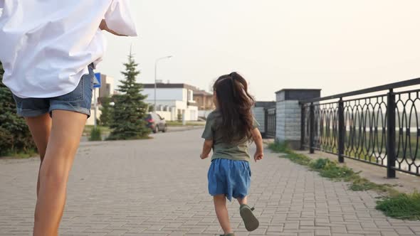 Playful Young Woman with Daughter Runs Along Embankment