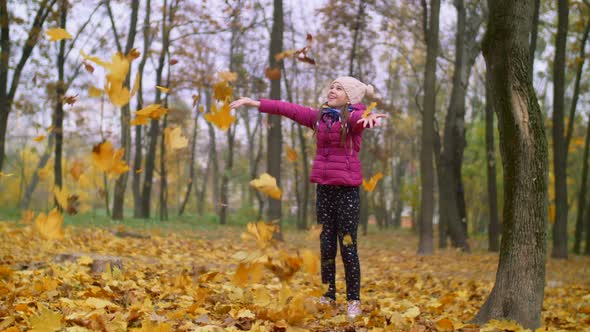 Joyful Girl Tossing Autumn Foliage Up Outdoors