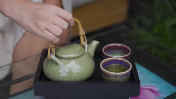 A close up shot of a women's hands pour hot drinks in the cup from a kettle. The kettle and cups wer