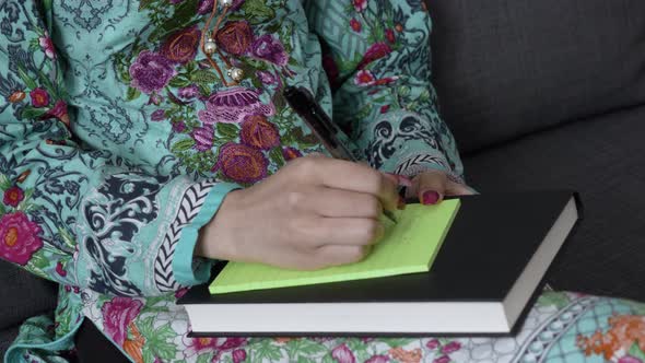 Medium Close Up of Young Asian Indian female's hand in salwar kameez writing down notes with pen sit