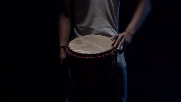 Black Man Drummer Plays with Hands on an African Drum in the Studio in Dark