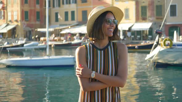 A woman with watch, hat, sunglasses, striped dress traveling, Portofino, Italy, luxury resort Europe