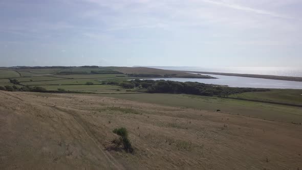 Low forward tracking aerial down a hill towards the fleet lagoon at the west end of Chesil Beach. Ab