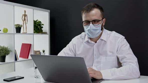 Handsome Businessman in Protective Mask Working Remotely at Laptop on Quarantine