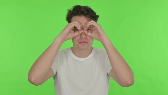 Searching Young Man with Binocular Gesture on Green Background
