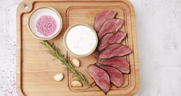 Grilled Rare Medium Beef Meat with Garlic and Rosemary in a Woden White Plate