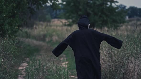 Backside portrait of death in nature. Dark figure in black costume out stretches its arms