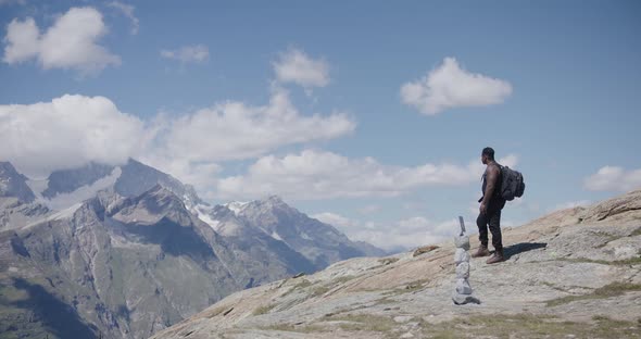 Black male traveler crossing himself and walking away from mountainside edge near the Matterhorn in