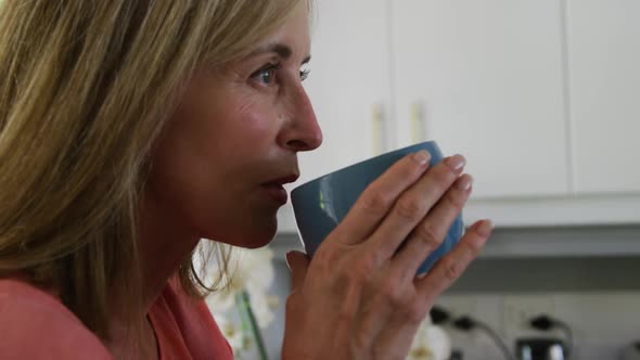 Caucasian senior woman standing in kitchen at home drinking cup of coffee