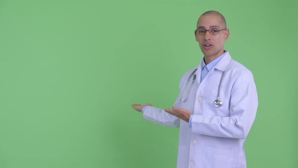 Happy Bald Multi Ethnic Man Doctor Talking While Showing To Back