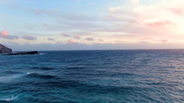 Drone flying close above the waves during sunrise with mini tropical islands in view