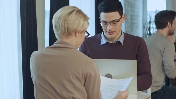 Young Businessman Working on Laptop and Businesswoman Working with Documents Sitting at the Desk