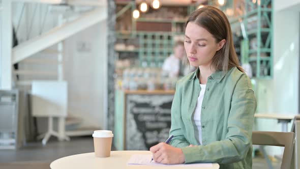 Woman Thinking and Writing on Paper in Cafe