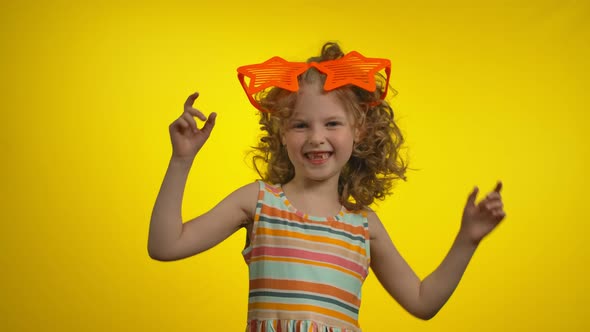 Little Curly Girl in Funny Star Glasses with Charming Toothless Smile is Dancing