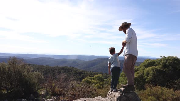 A father and son stand on a cliff overlooking the great dividing range.