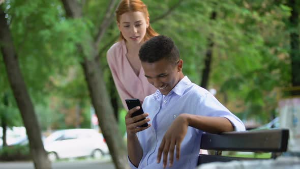 Offended Teen Girl Noticing Her Boyfriend Chatting Smartphone in Park, Jealousy