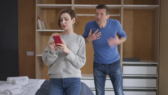 Absorbed Wife Surfing Social Media on Smartphone Ignoring Husband Gesturing Shouting at Background