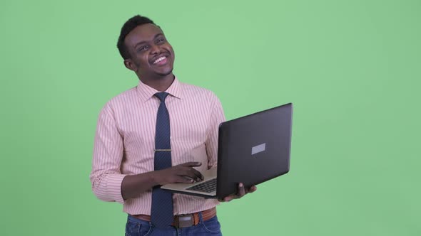 Happy Young African Businessman Thinking While Using Laptop