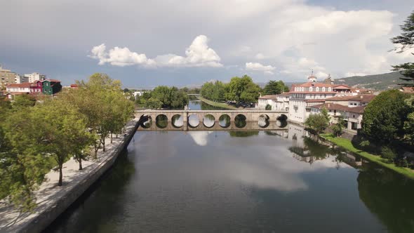 Fly over Tamega river and picturesque Roman Bridge, Chaves, Portugal. Clouds reflected on calm water