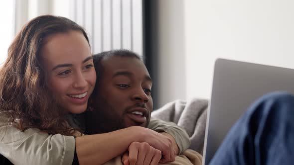 Relaxed Young Couple At Home Sitting On Sofa Browsing Internet On Laptop Computer