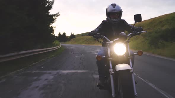 Close Up Front View of Driver Riding Motorcycle on an Asphalt Road Through Forest