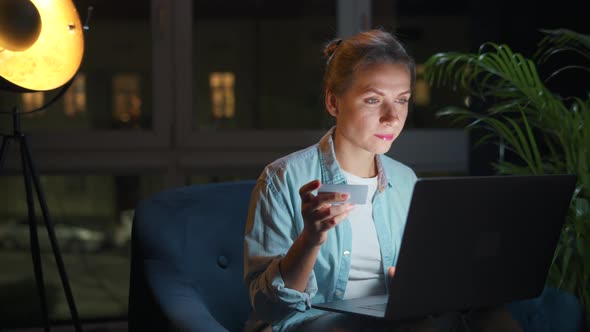 Woman is Sitting in the Armchair and Makes an Online Purchase Using a Credit Card and Laptop at