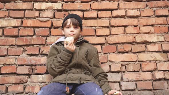 Street Kid Boy Sits on the Concrete Outdoors Looking at Camera Having No Home