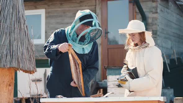 Man and Woman Beekepers Inspecting Beehive Outdoors
