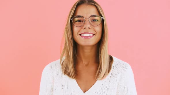 Young Woman in Glasses and White Jumper is Winking Showing Hand Gesture Okay Smiling While Posing on