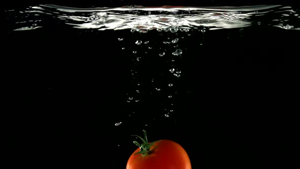 Slo-motion whole tomato rising after falling through water