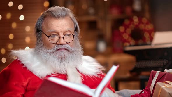 Wondered Male Santa Claus with Natural Beard Reading Red Paper Book Wish List