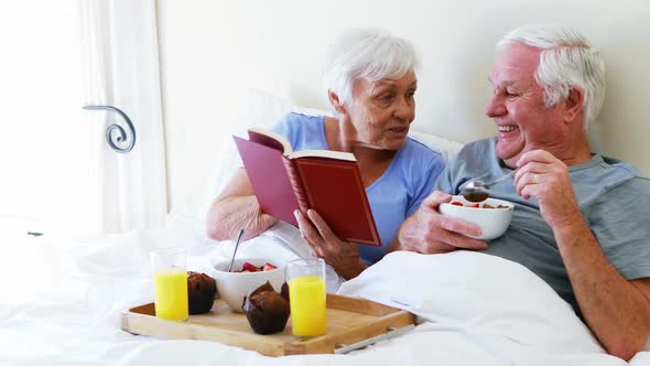 Senior couple interacting with each other while having breakfast on bed