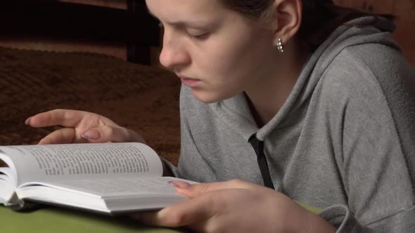 Beautiful Girl Reads a Book Comfortably While Lying in Bed