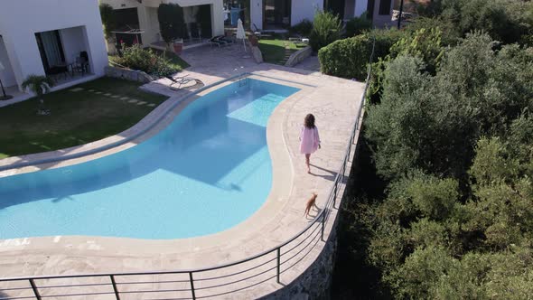 Drone footage of woman walk near swimming pool, and Modern Villas in scenic countryside.