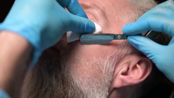 Barber correcting beard of an adult man, close-up. Working with a straight razor