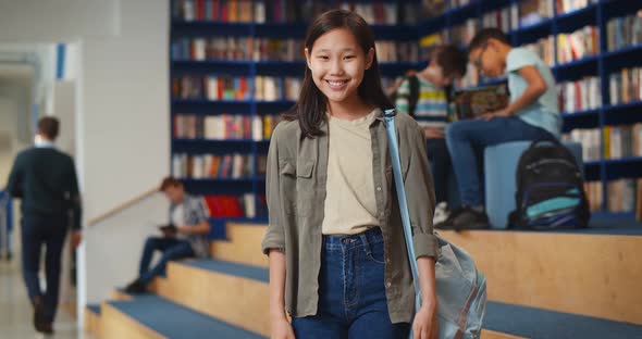 Portrait of Smiling Asian Schoolgirl Looking at Camera Standing in Library