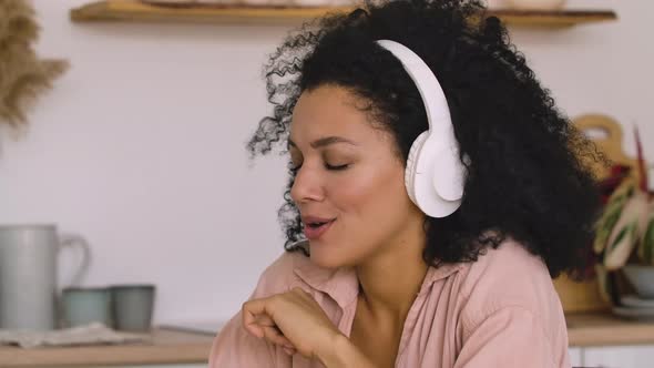 African American Woman in Big White Headphones Listens to Music with Pleasure Using Smartphone